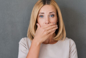 a woman covering her mouth with her hand because she has missing teeth and needs to replace them with dental implants.
