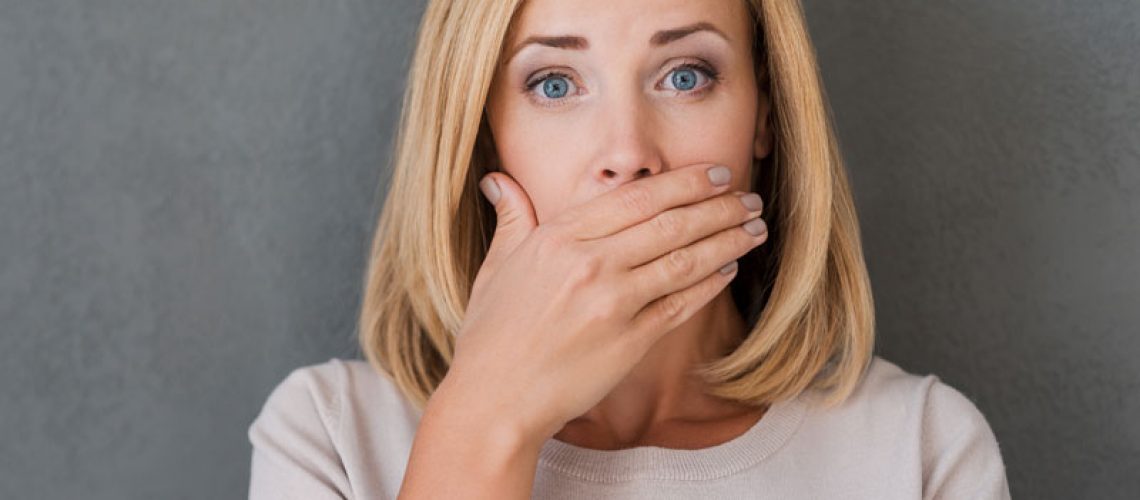 a woman covering her mouth with her hand because she has missing teeth and needs to replace them with dental implants.